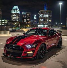 a red sports car parked in front of a city skyline at night with lights on