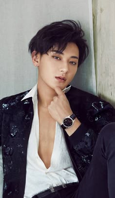 a young man wearing a black jacket and white shirt is leaning against a wall with his hand on his chin