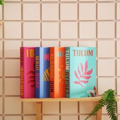 four books are on a shelf in front of a tiled wall and a potted plant