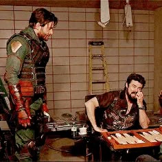 two men in costumes are sitting at a table and one man is talking on the phone