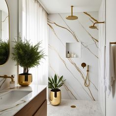 a white bathroom with gold accents and marble counter tops, along with a plant in the corner