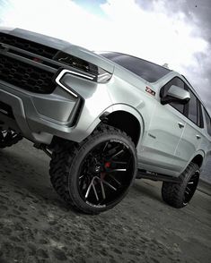 a silver truck parked on top of a sandy beach next to the ocean and cloudy sky