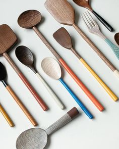 various wooden spoons and spatulas lined up on a white surface with different colored handles