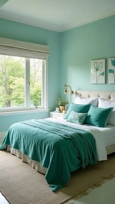A serene bedroom featuring a light teal color scheme, neatly made bed with teal and white pillows, and modern wall art, framed by a sunny window overlooking greenery.