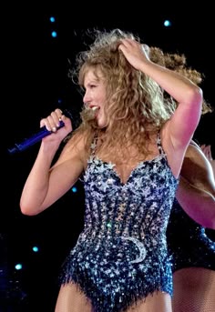 a woman in a bodysuit holding a microphone and singing into the air with her hands behind her head