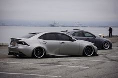 two cars parked next to each other in a parking lot near the water and people