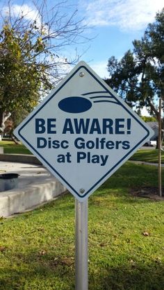 a sign that says be aware disc golfers at play in front of a park