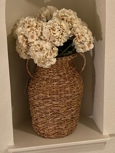a wicker vase with white flowers in it on a shelf next to a wall