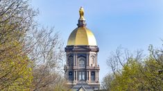a large building with a golden dome in the middle of trees and blue sky behind it