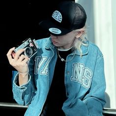 a person sitting down holding a camera and wearing a denim jacket with the number 17 on it