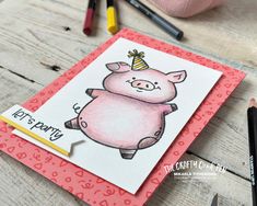 a pink pig with a party hat on it's head sitting next to some crayons