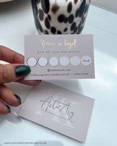 a person holding up a business card on top of a white table next to a cup