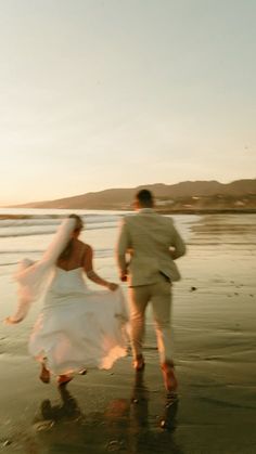 a bride and groom running on the beach
