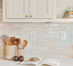 an open book sitting on top of a counter next to wooden spoons and utensils