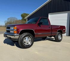 a red pick up truck parked in front of a building with a garage door open