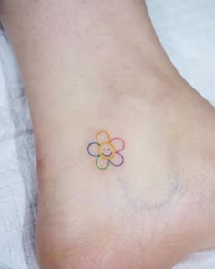 a small flower tattoo on the foot of a person's left foot, with a smiley face drawn on it