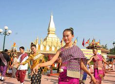 some people are dancing in front of a large building with flags on the sides and one is wearing a purple dress