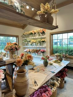 a room filled with lots of flowers and vases on top of a wooden table