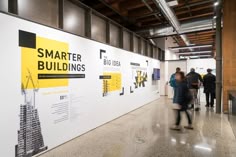 people are walking around in an art gallery with posters on the wall and below them
