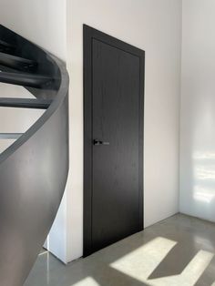 a black door in a white room next to a spiral staircase