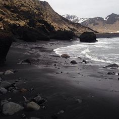 the beach is covered in rocks and water near some mountain peaks with snow on them