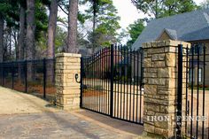an iron fence and gate in front of a house with trees around the entrance area