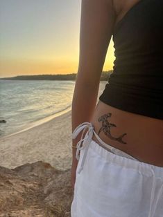 a woman with a tattoo on her stomach standing by the beach at sunset or sunrise
