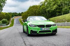a green car driving down a road next to some grass and trees in the background