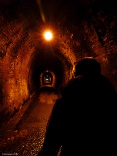 a man is walking through a dark tunnel with light at the end and his head turned to the right