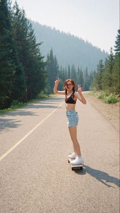 a woman riding a skateboard down the middle of a road with trees in the background