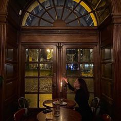 a woman sitting at a table with a lit candle in her hand and looking out the window