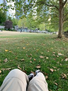 someone is laying down in the grass with their feet on the ground and trees behind them
