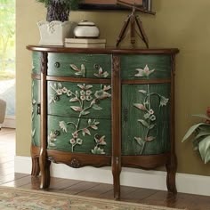 an ornate green cabinet with flowers painted on it's doors and drawers in a living room