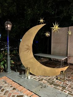 a large crescent shaped sculpture sitting on top of a brick walkway next to a bench