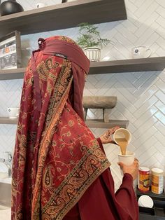 a woman in a red shawl is pouring something into a cup on the counter