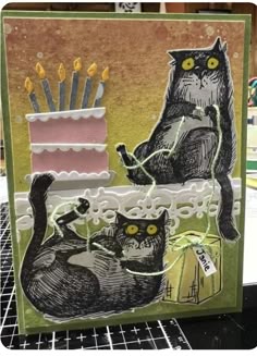a card with two cats and a birthday cake on it, one has candles in the background