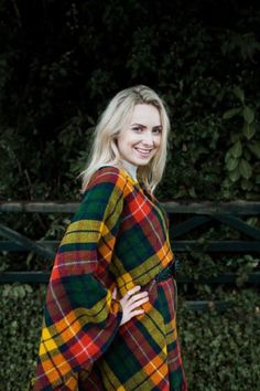 a woman standing in front of a fence wearing a plaid coat and jeans with her hands on her hips