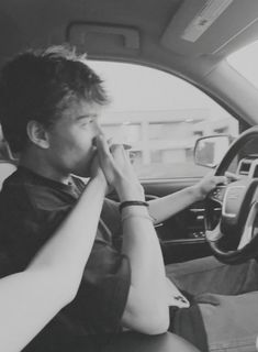 a man sitting in the driver's seat of a car while holding his hand to his mouth