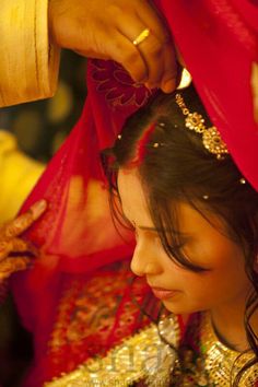 a woman getting her hair combed by a man in a red shawl and gold jewelry