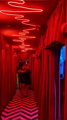 two people are standing in the middle of a room with red curtains and black and white chevron flooring
