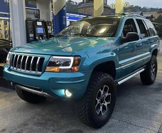 a blue jeep is parked in front of a gas station with its lights turned on
