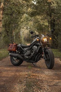 a black motorcycle parked on the side of a dirt road in front of some trees