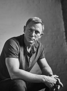 a black and white photo of a man sitting on a chair looking at the camera