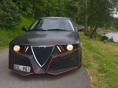 a black car parked on the side of a road next to a lake and trees