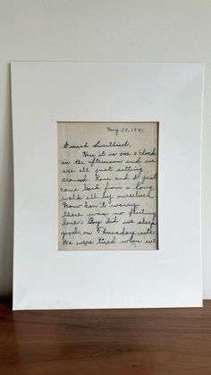 a handwritten letter is framed in a white frame on a wooden table next to a wall