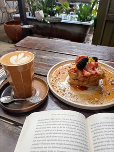an open book sitting on top of a wooden table next to a cup of coffee