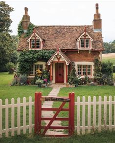 a red gate in front of a house with a white picket fence and green grass