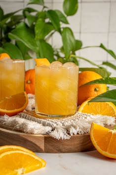 two glasses filled with orange juice next to sliced oranges and green leaves on a table
