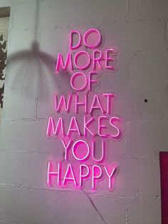 a pink neon sign that says do more of what makes you happy on a white brick wall