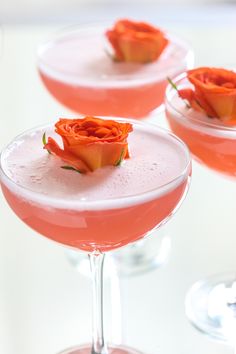 three glasses filled with pink liquid and topped with orange flowered stem garnish